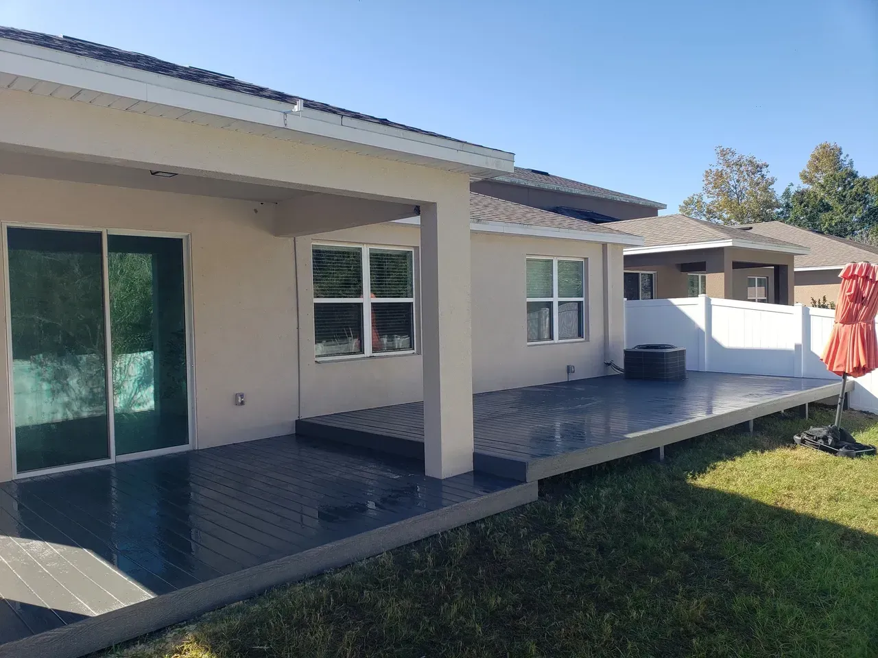 The backyard of a house with a patio and a red umbrella.