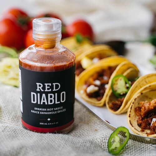 A bottle of red diablo sauce next to a plate of tacos