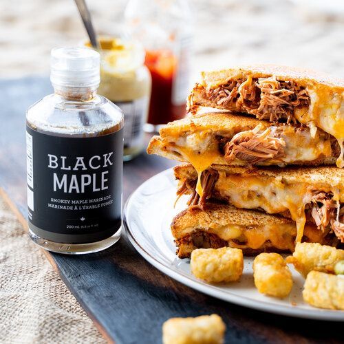 A stack of grilled cheese sandwiches on a plate next to a bottle of black maple sauce.