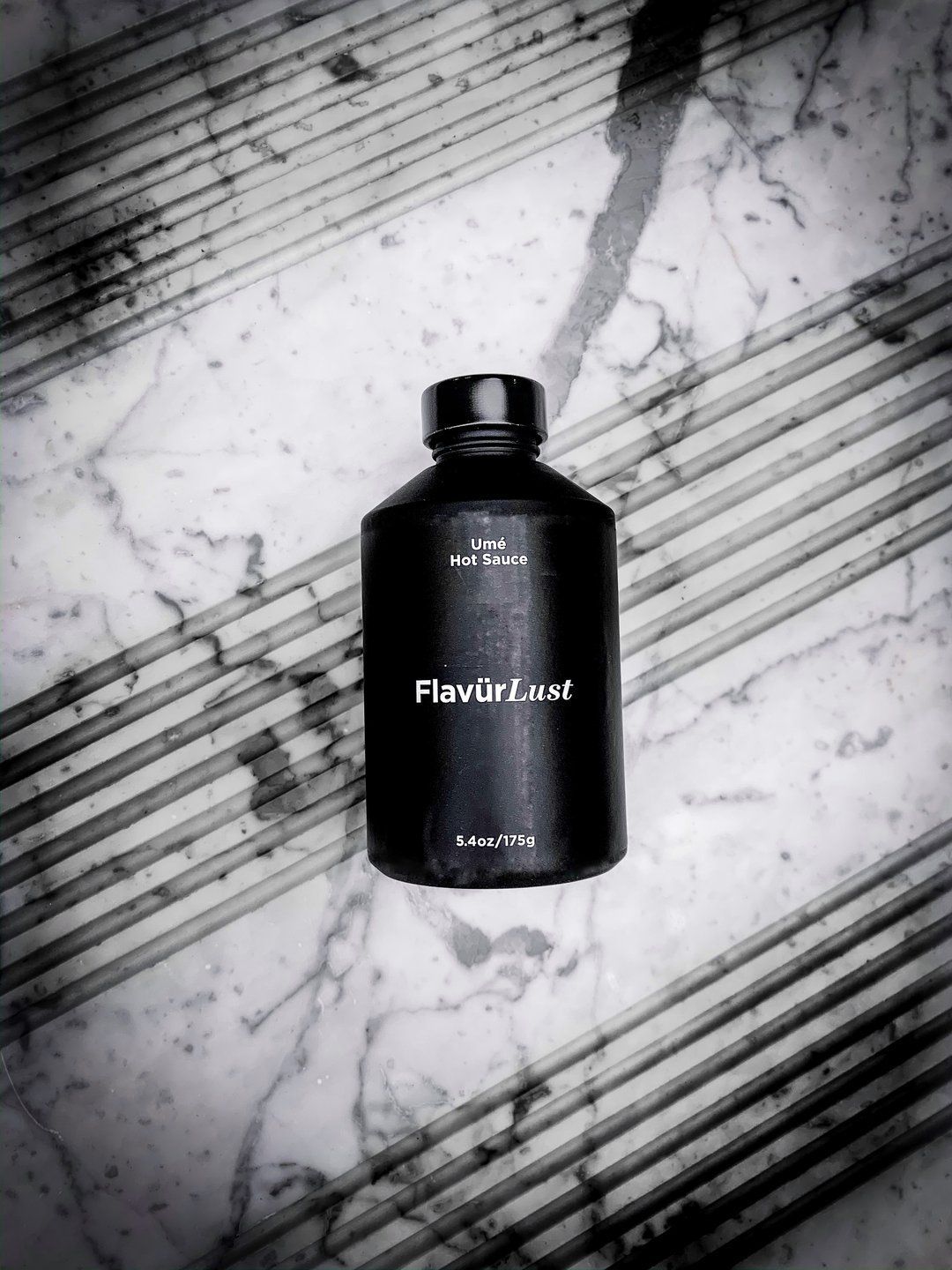 A black bottle of perfume is sitting on a marble surface.