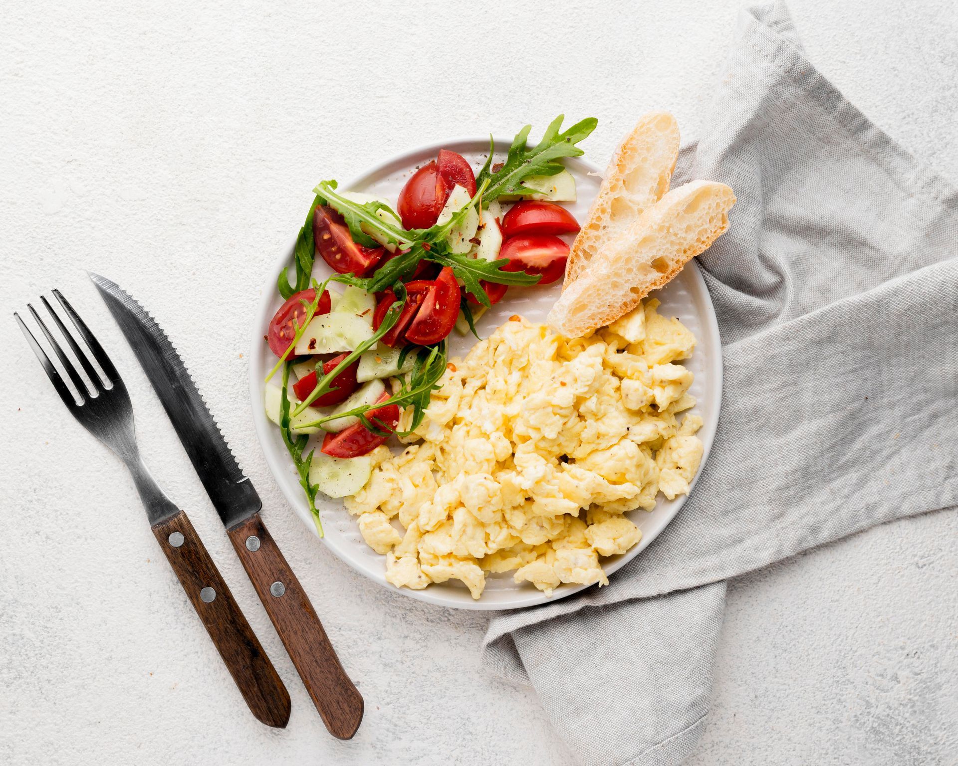 A plate of food with scrambled eggs , tomatoes , cucumbers and bread