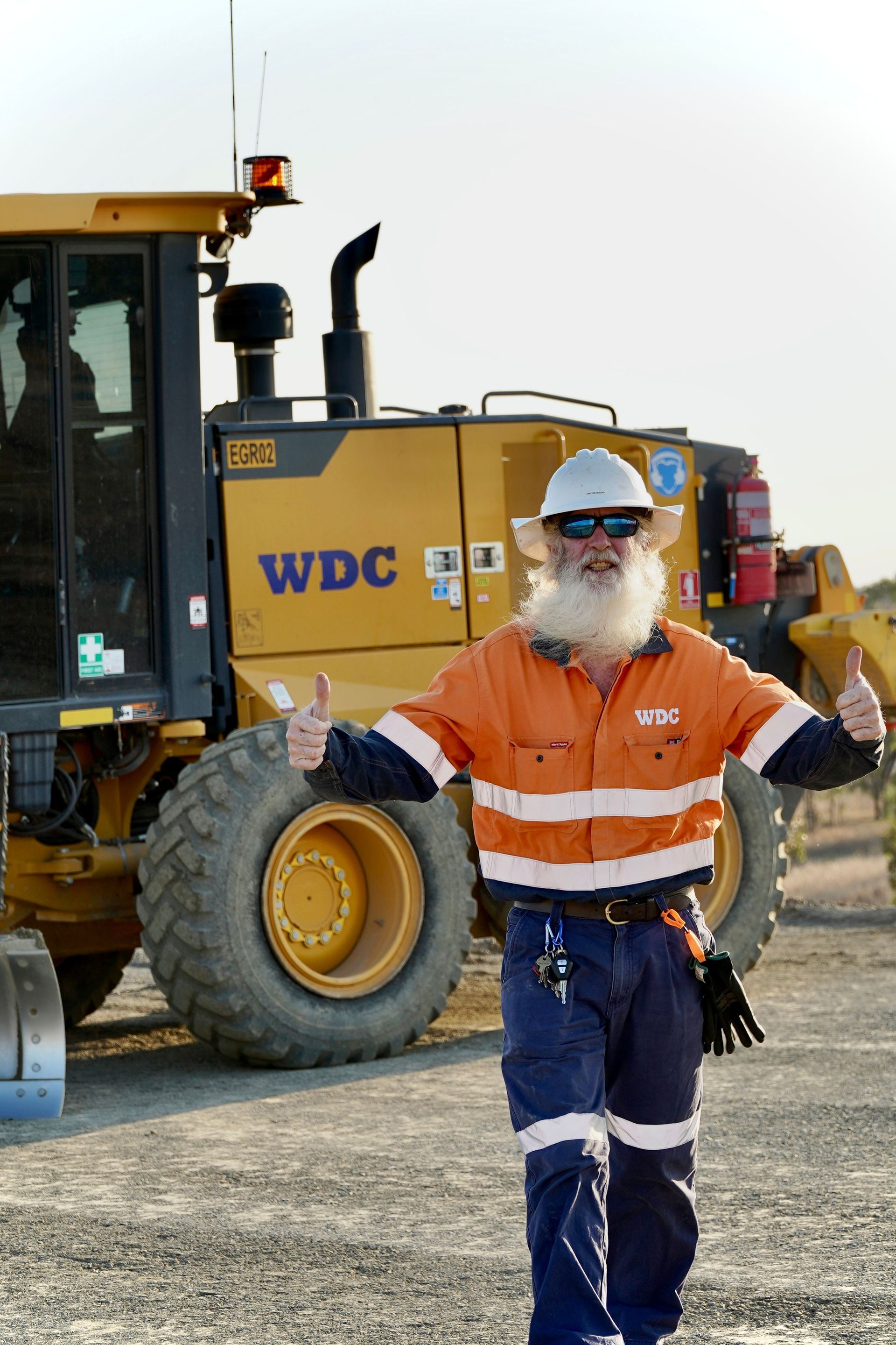 Worker in hard hat and reflective vest standing in front of a construction vehicle at a gravel site