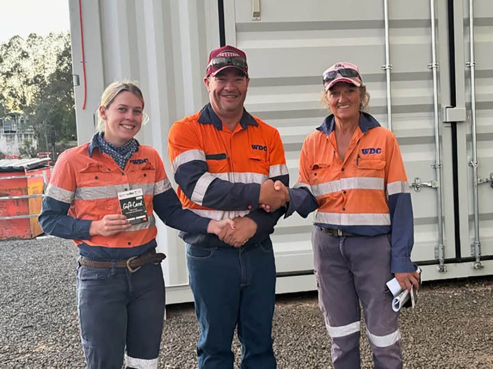 Three workers in orange safety uniforms standing and smiling at a work site
