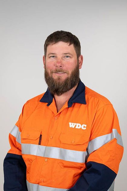 Man in an orange and navy high-visibility work shirt against a plain gray background.