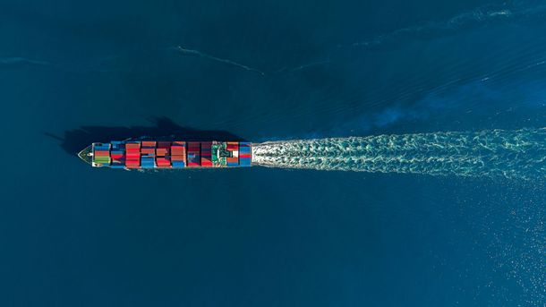 Nave mercantile che naviga nell'oceano blu profondo, lasciando una scia bianca.