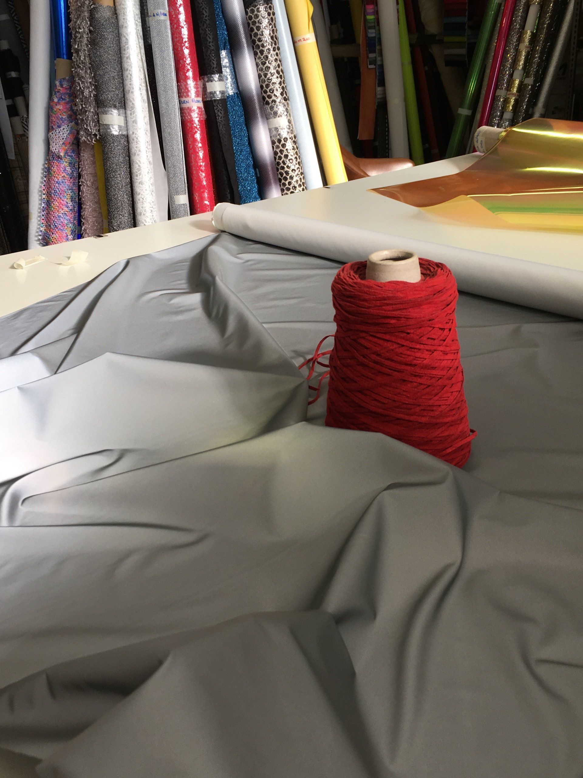 Una bobina di filo rosso è appoggiata sopra un pezzo di tessuto