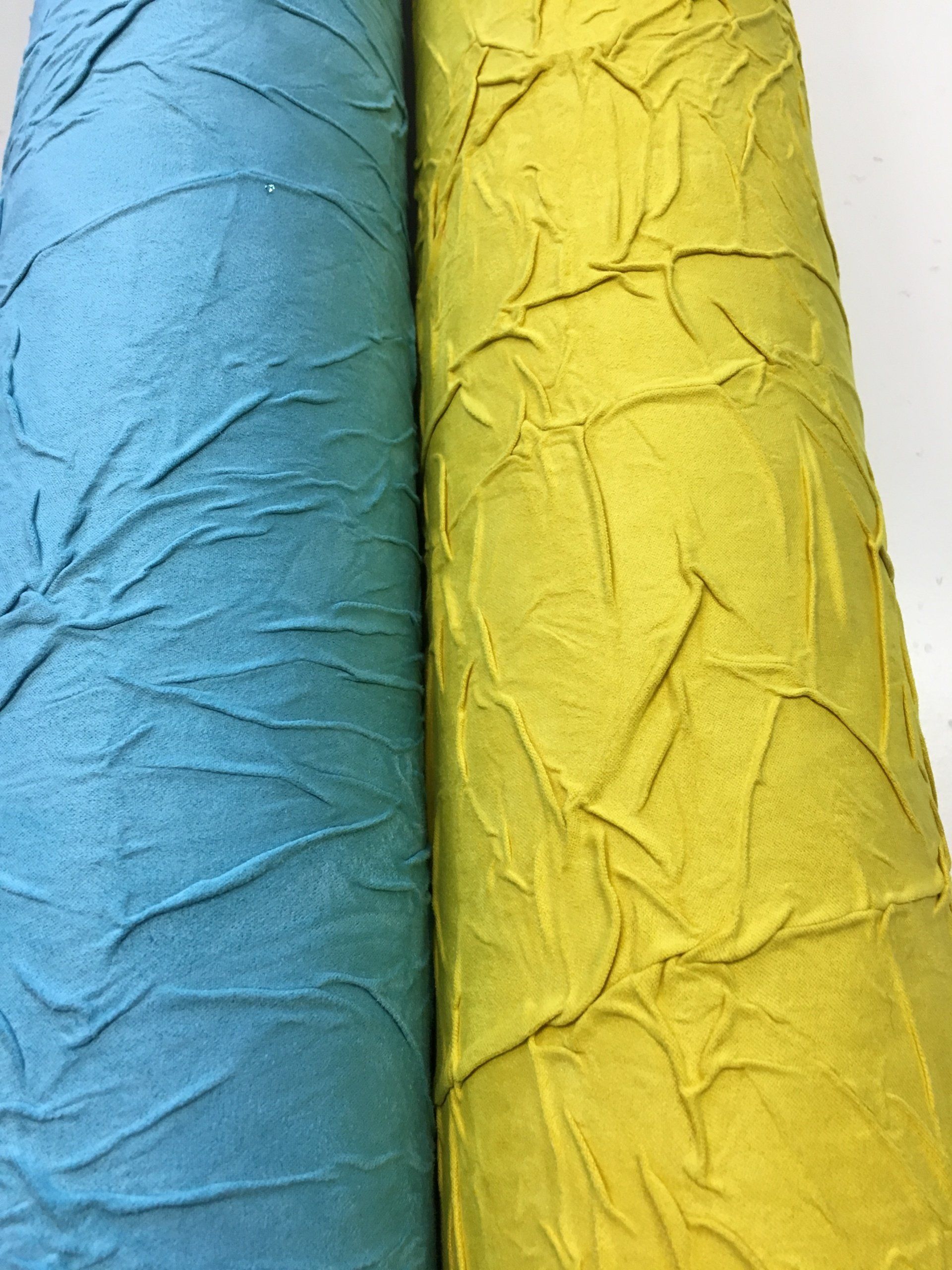 Due rotoli di stoffa, uno blu e uno giallo, sono appoggiati uno accanto all'altro su un tavolo.