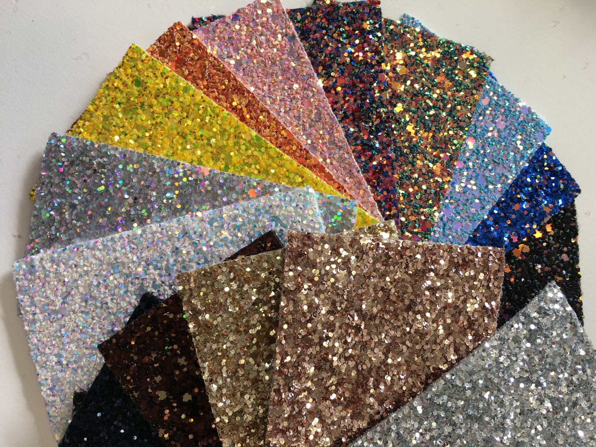 Un mucchio di fogli di brillantini di diversi colori sono impilati uno sopra l'altro su un tavolo.