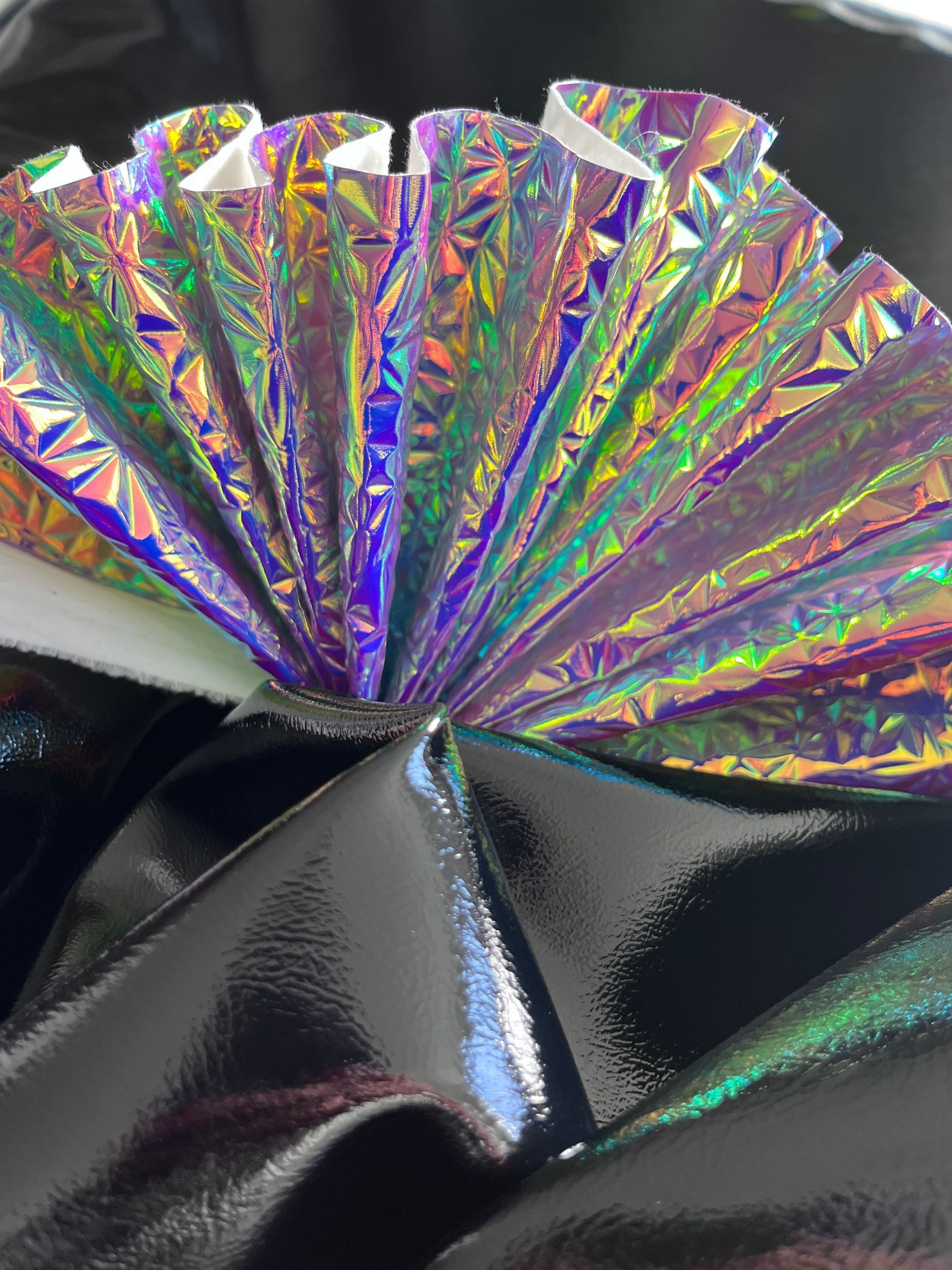 Primo piano di un ventaglio fatto di carta olografica su una superficie nera.