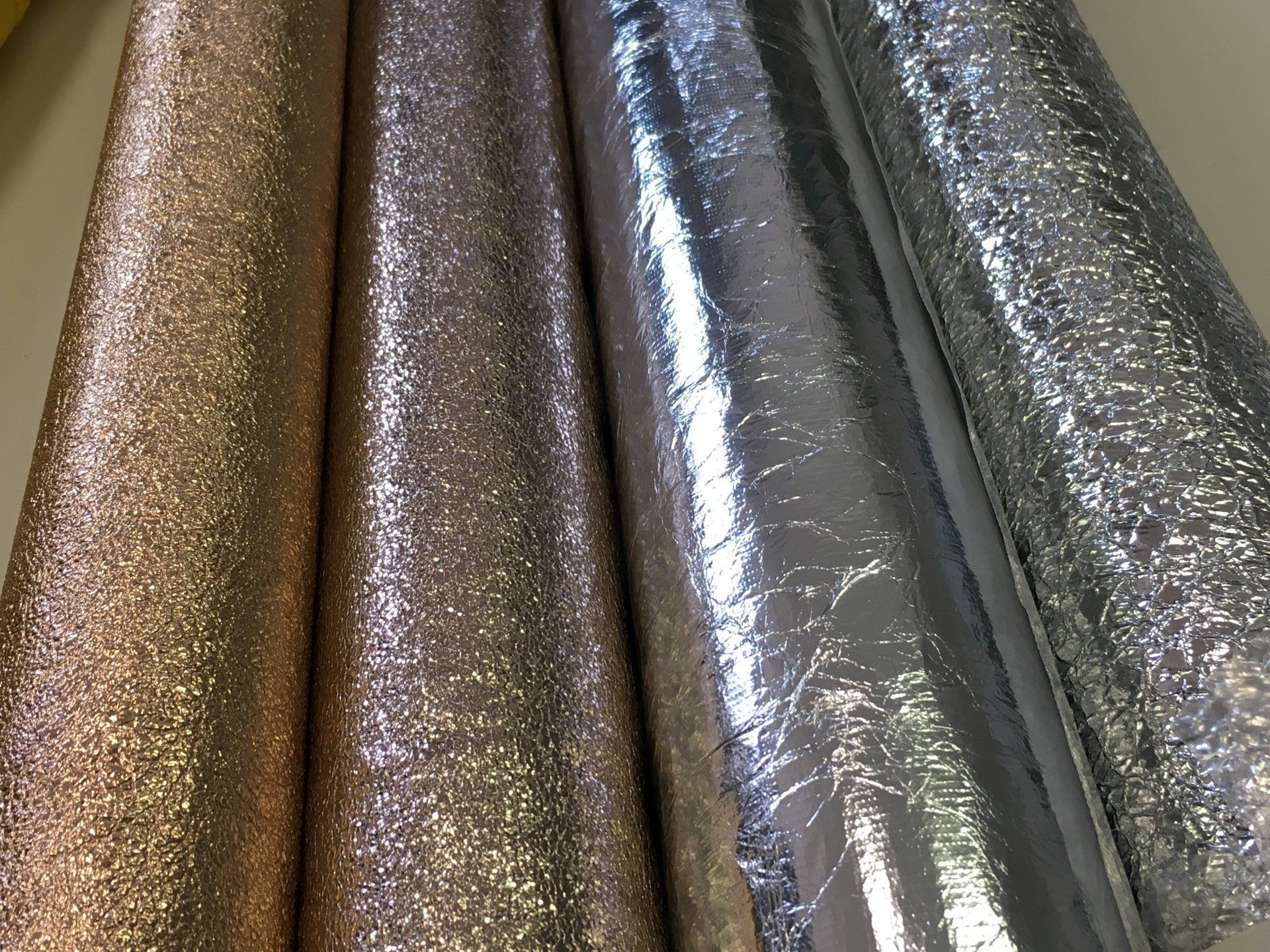 Tre rotoli di carta glitterata sono appoggiati su un tavolo.