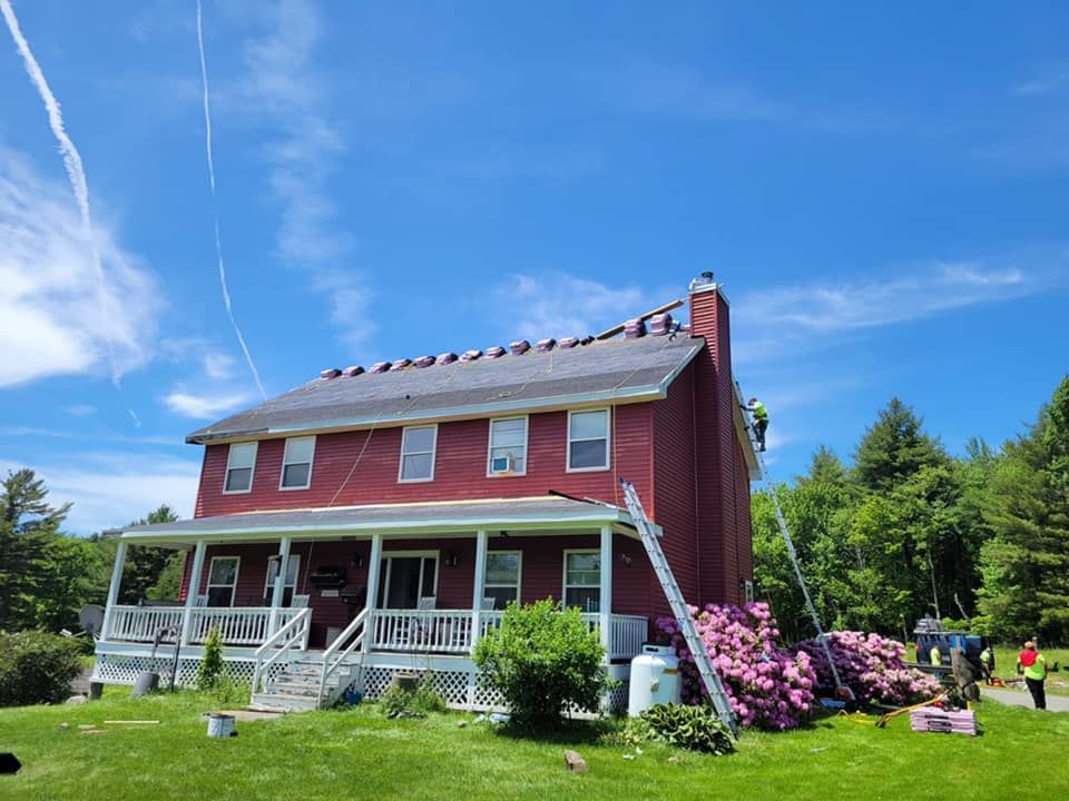 A red house with a roof being installed on a sunny day.