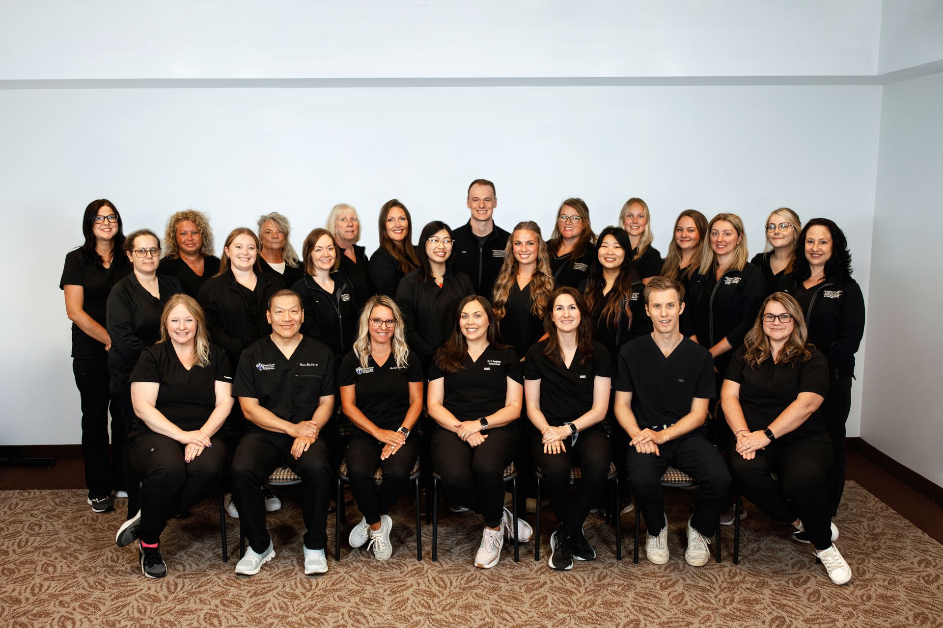 Group photo of dental office staff, all in black, posing together in front of a plain wall. Group photo of dental office staff, all in black, posing together in front of a plain wall.