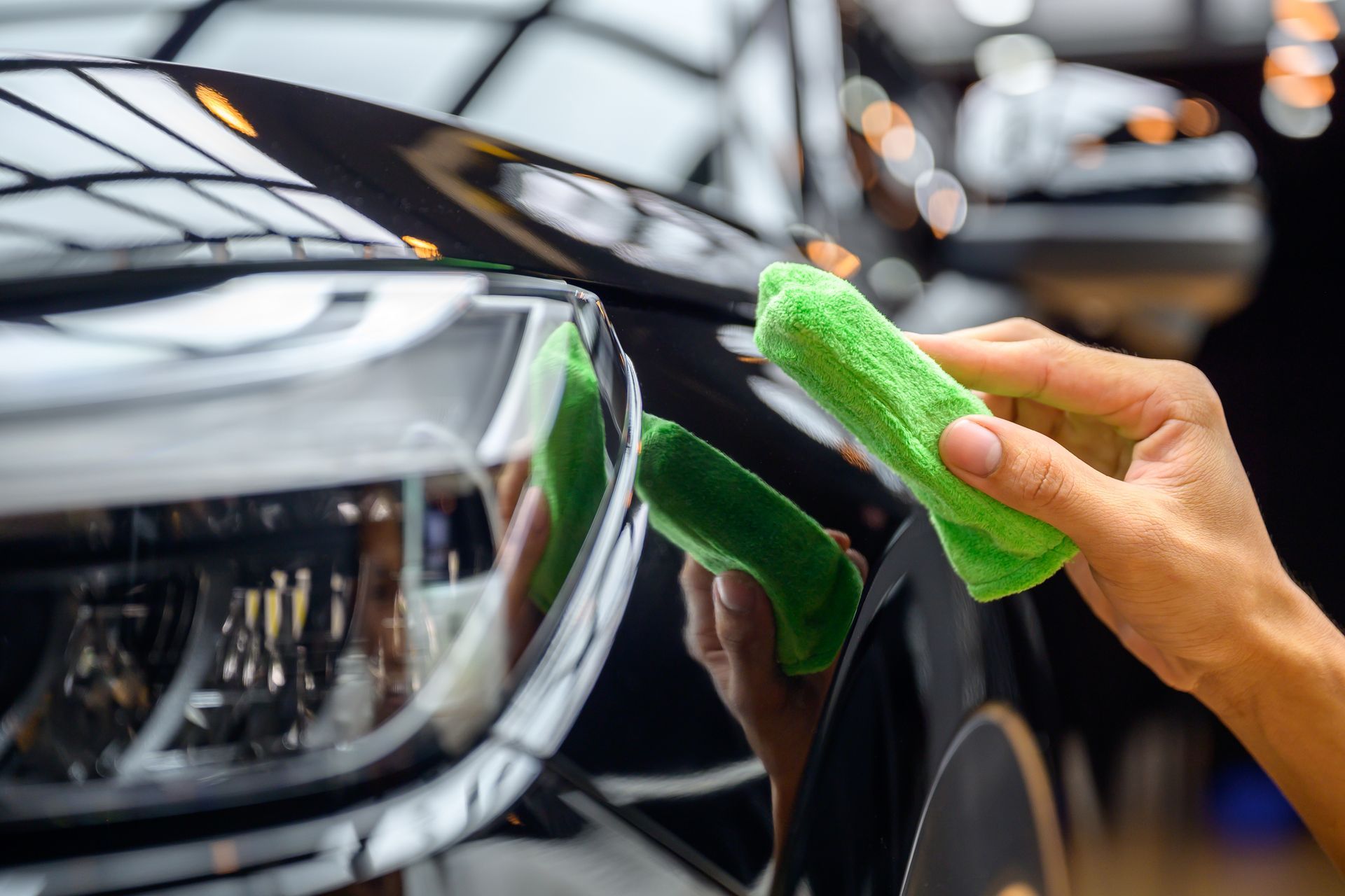 A person is cleaning a car with a green cloth.