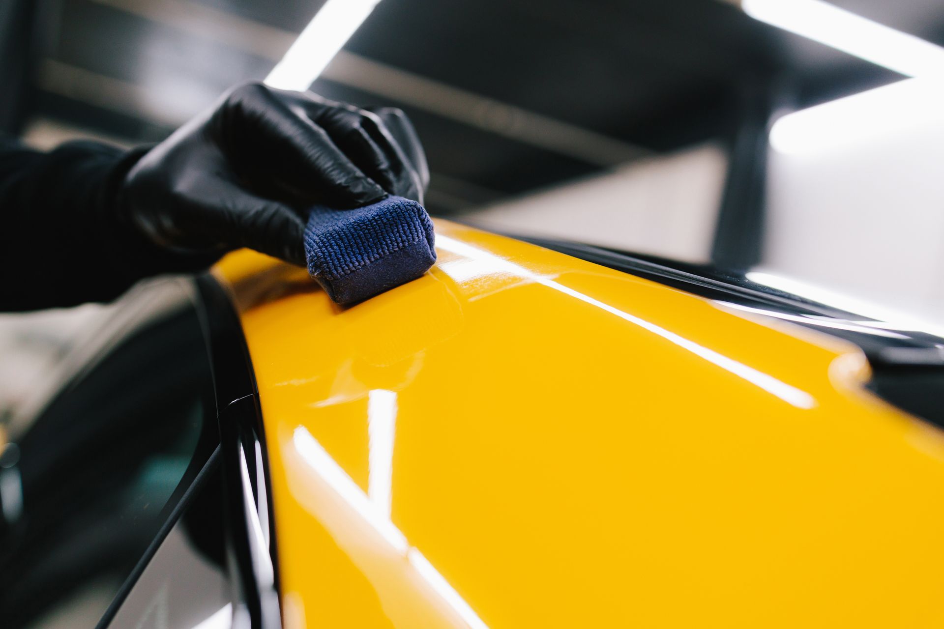 A person is polishing a yellow car with a sponge.