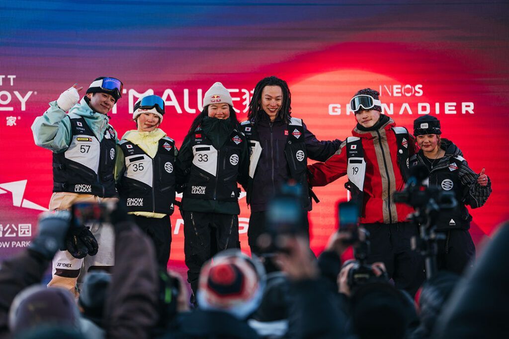 Sechs Snowboarder mit Trophäen auf einem Podium, die vor einem roten Hintergrund feiern.