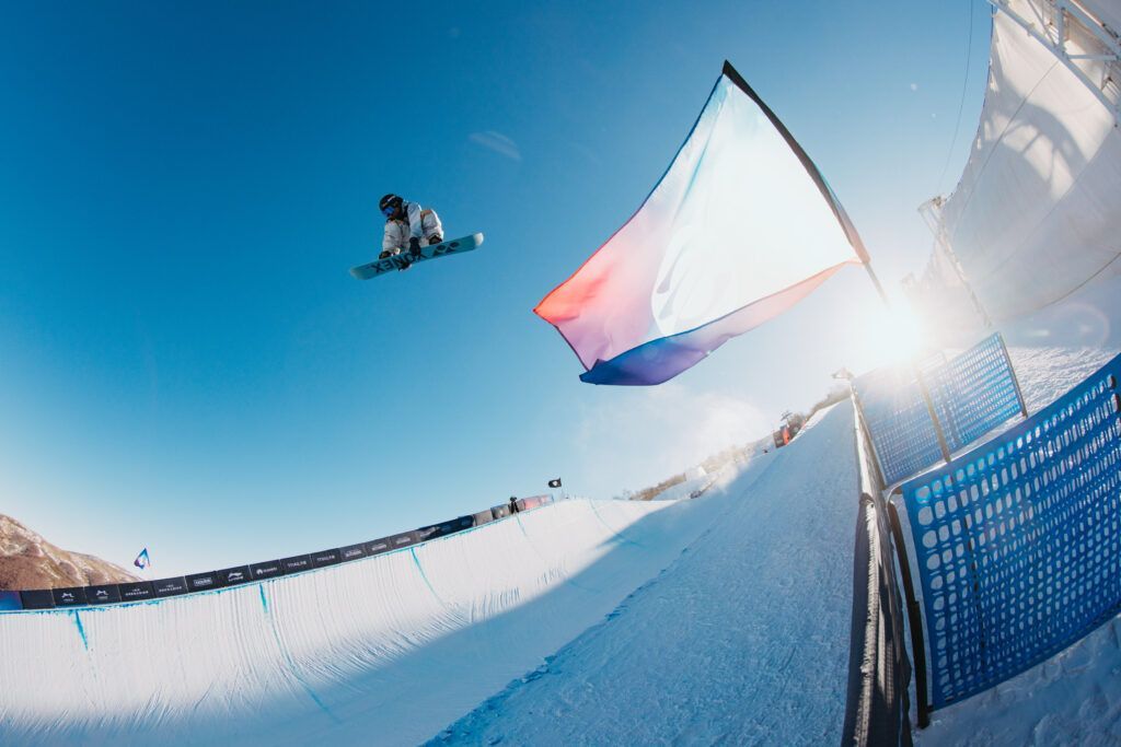 Snowboarder in der Luft, Fahne schwenkend, vor strahlend blauem Himmel auf einem schneebedeckten Hang.