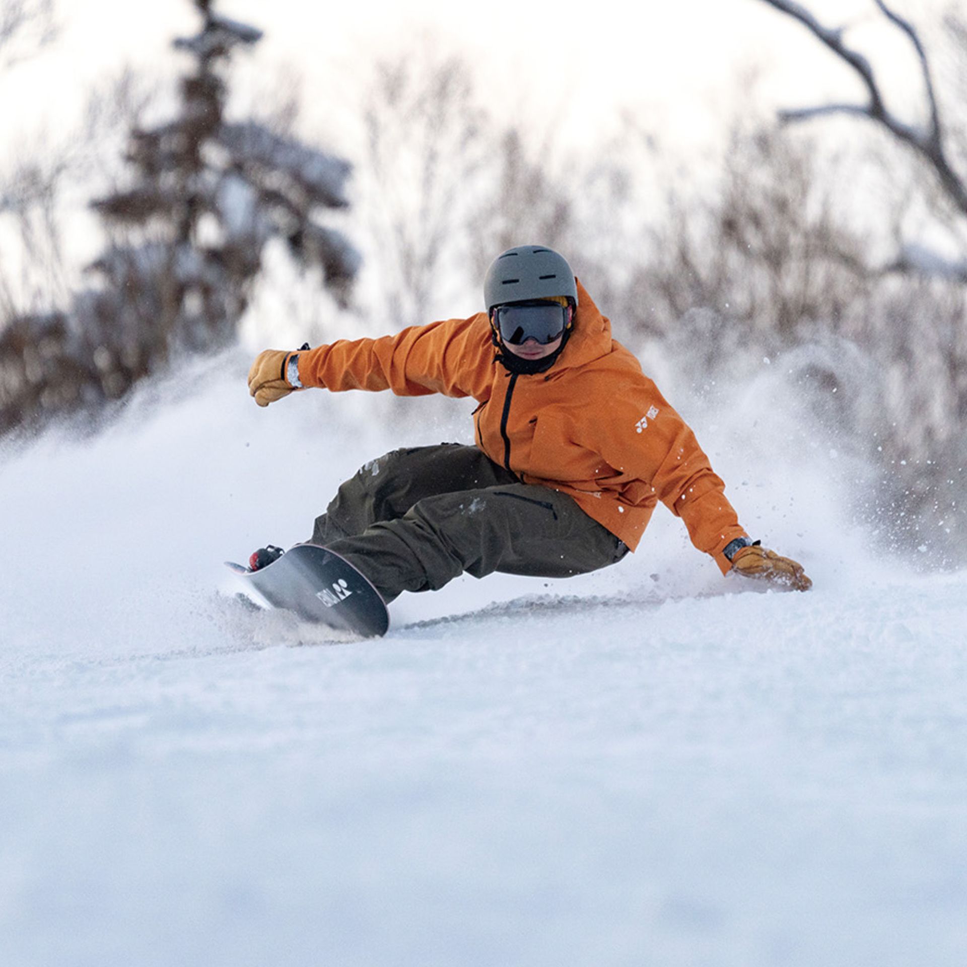 Ein Snowboarder mit Helm und Schutzbrille fährt einen schneebedeckten Hang hinunter