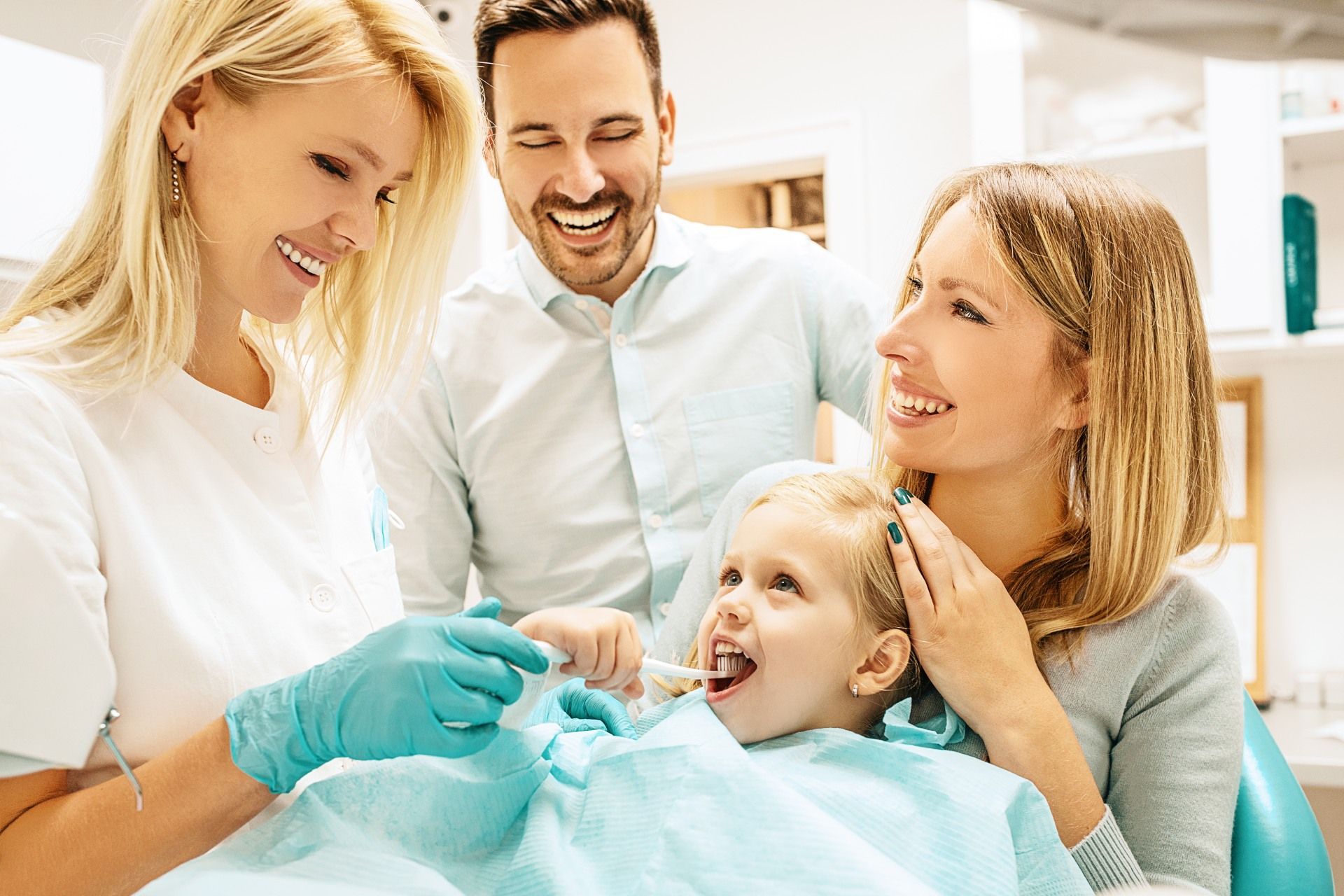A little girl is getting her teeth examined by a dentist while her parents watch.