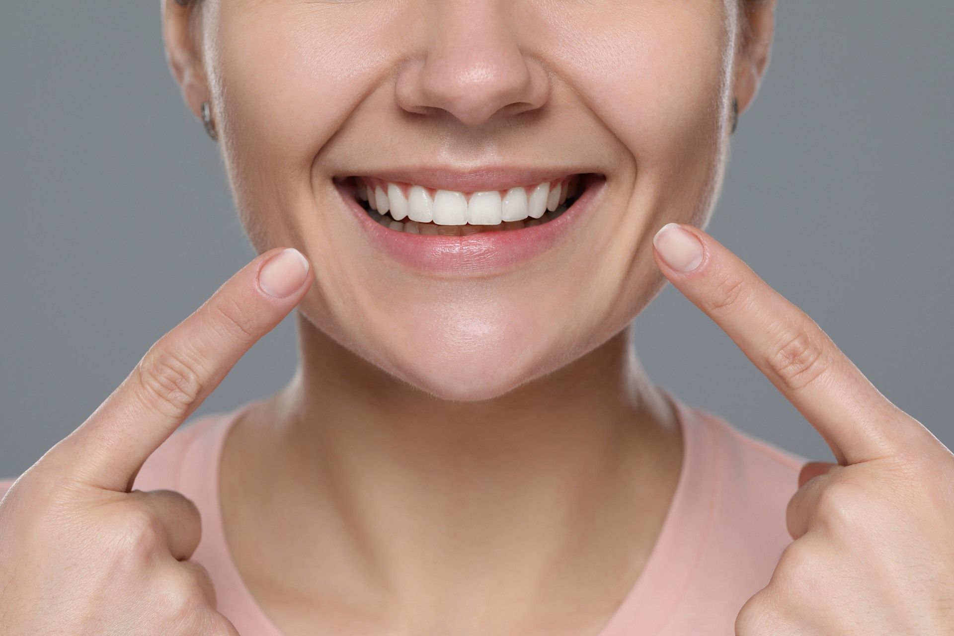 A woman is smiling and pointing at her teeth with her fingers.