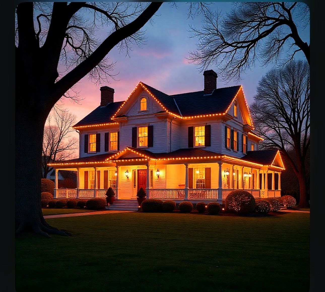 Two-story white house at dusk, illuminated with orange holiday lights, framed by trees and a colorful sky.