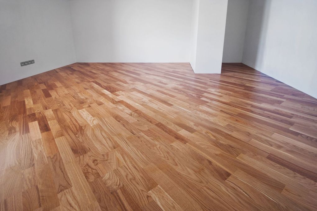 Empty room with light wood flooring and white walls, viewed from a corner.