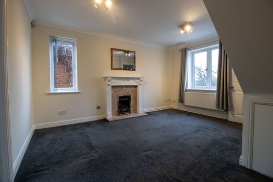 Empty living room with dark carpet, white fireplace, and two windows with curtains and blinds