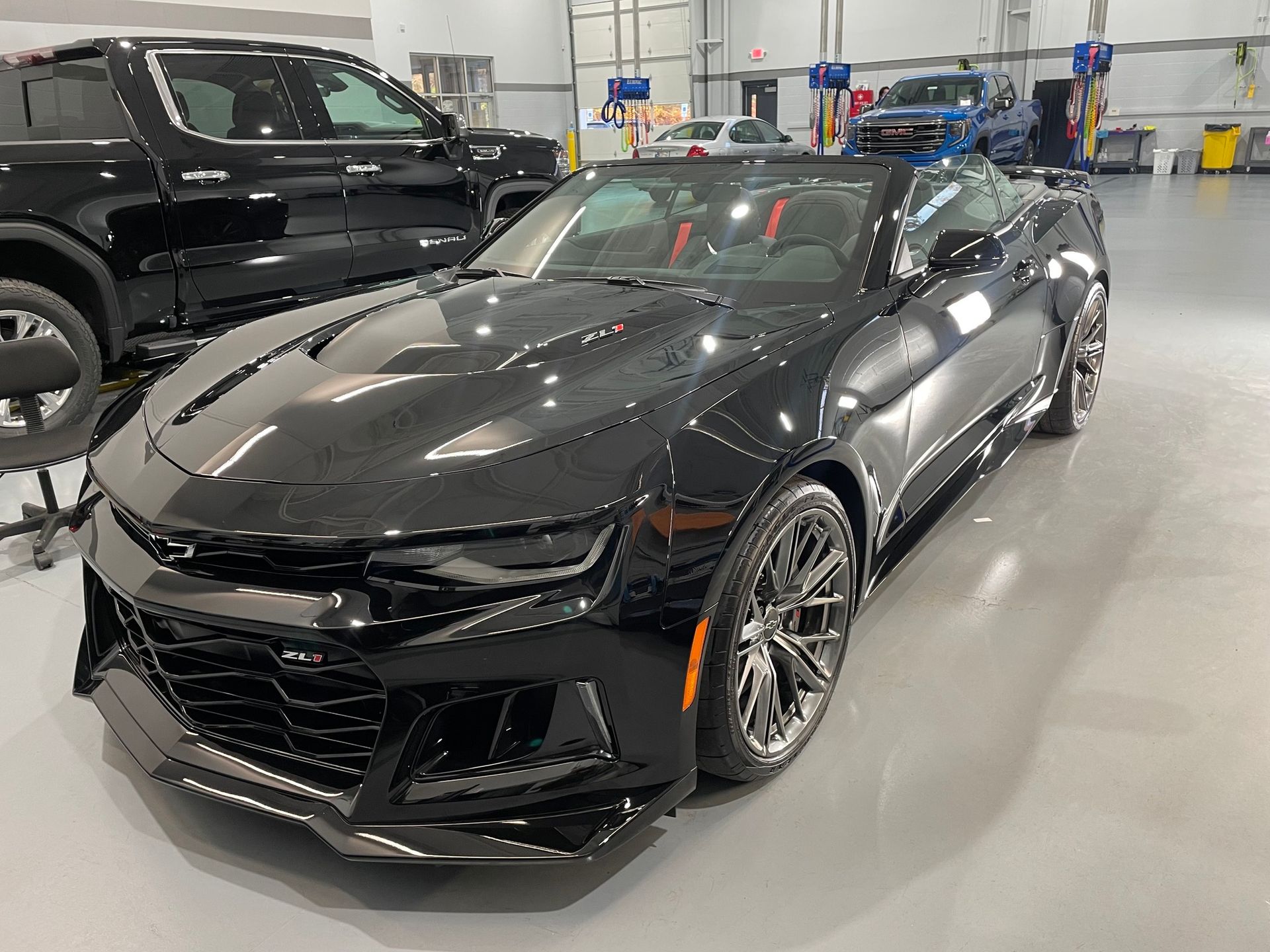 Black Chevrolet Camaro in a garage, next to a black pickup truck.