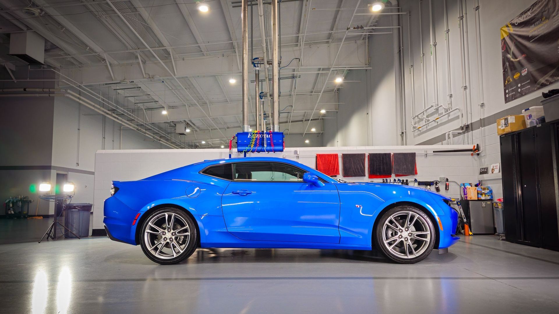 Blue sports car in a garage under a robotic arm.
