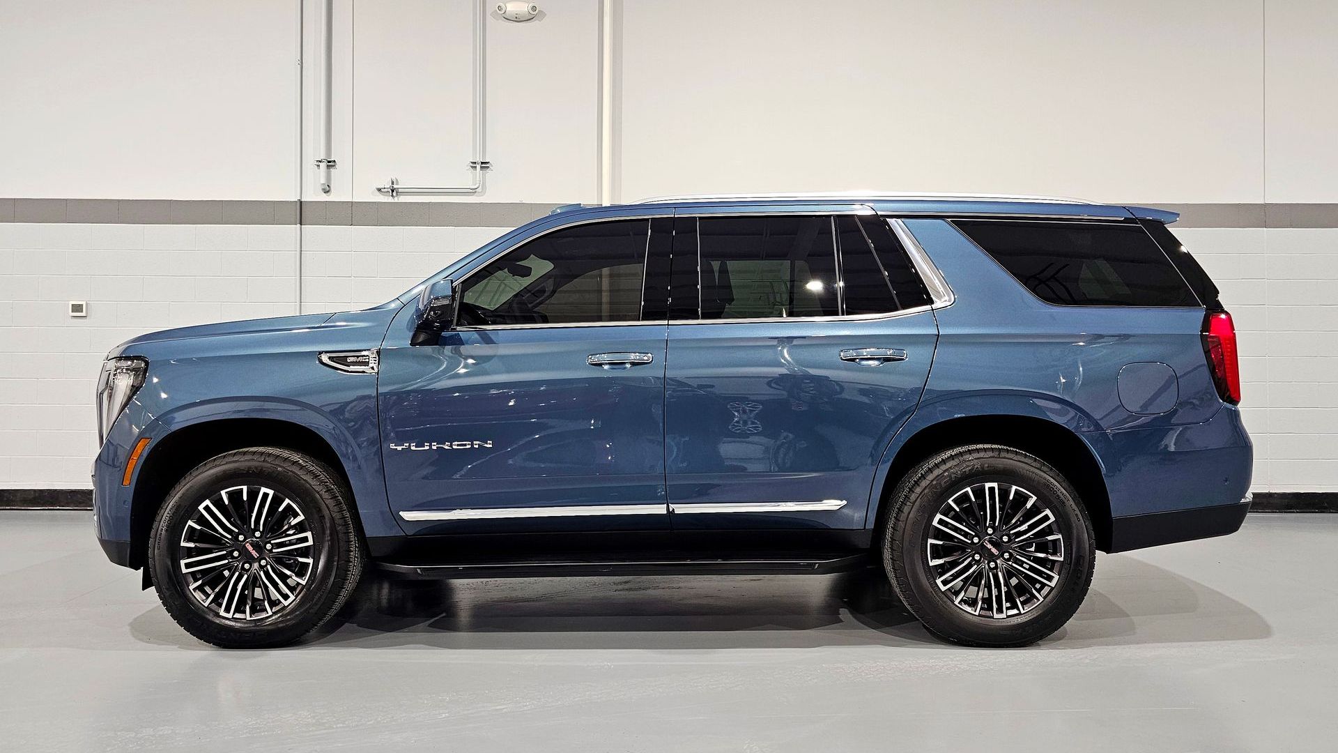 Blue GMC Yukon SUV parked in a garage with black and silver wheels.