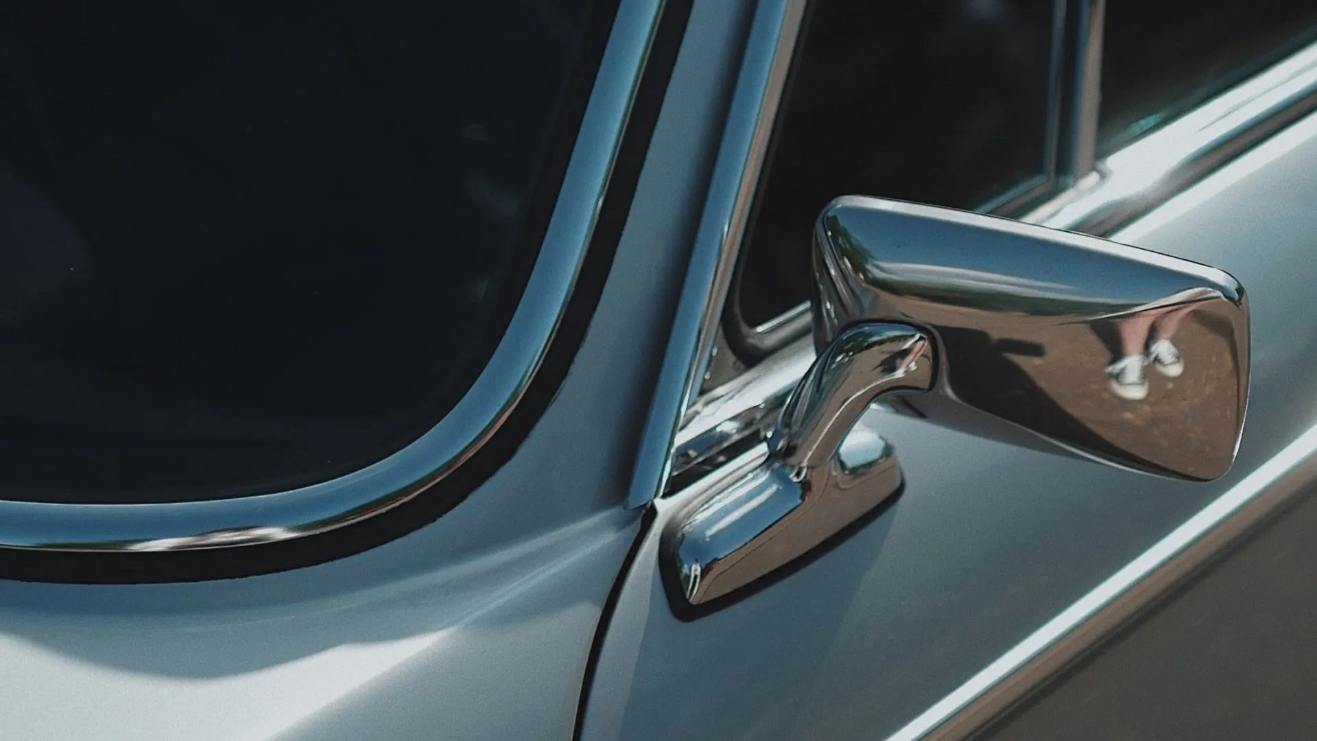Close-up of a chrome side mirror on a silver vintage car reflecting the surroundings.