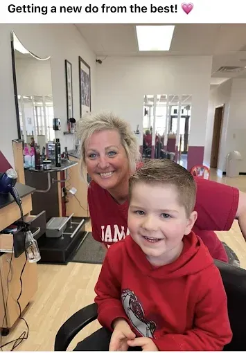 A woman is sitting next to a young boy in a barber shop.
