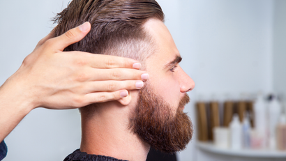 A man with a beard is getting his hair cut by a barber.