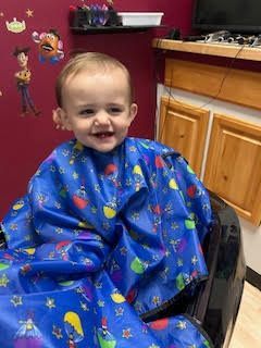 A little boy is sitting in a chair wearing a blue cape.