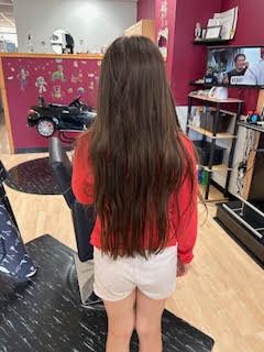 A little girl with long hair is standing in a barber shop.
