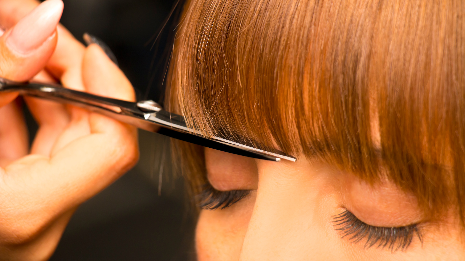 A woman is getting her hair cut by a hairdresser with scissors.