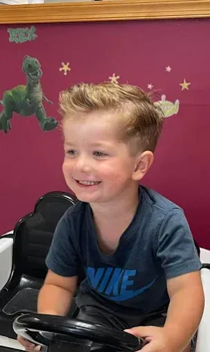 A young boy is sitting in a toy car and smiling.