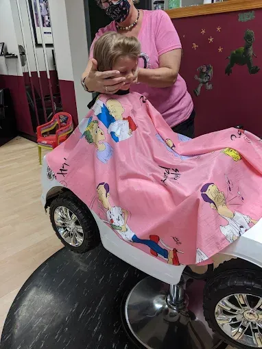 A little girl is getting her hair cut in a toy car.