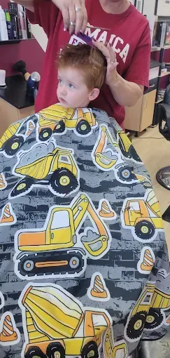 A little boy is getting his hair cut by a man in a barber shop.
