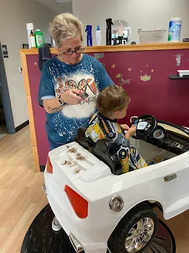 A woman is cutting a baby 's hair in a toy car.