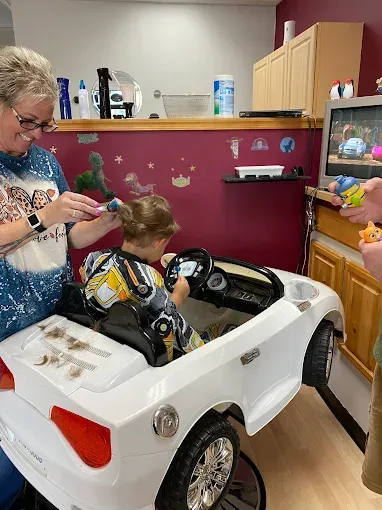 A little girl is getting her hair cut in a toy car.