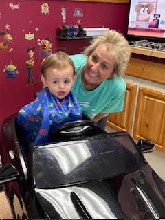 A woman is standing next to a toddler sitting in a toy car.
