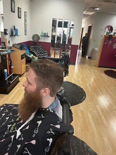 A man with a beard is getting his hair cut by a barber.