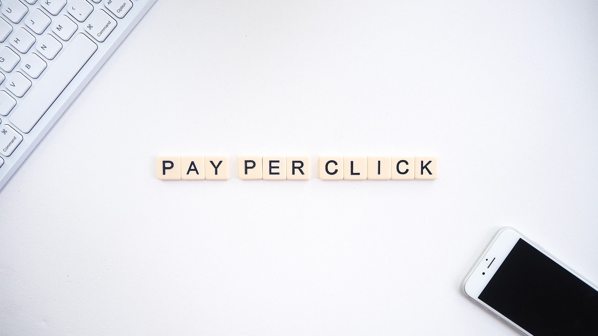 'Pay per click', spelt out using letter tiles. A laptop and mobile device are at the opposite edges of the image.