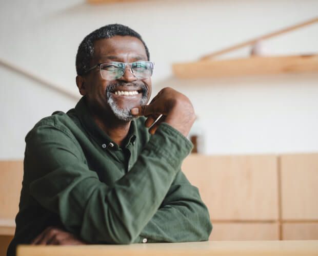a man wearing glasses and a green shirt is smiling while sitting at a table .