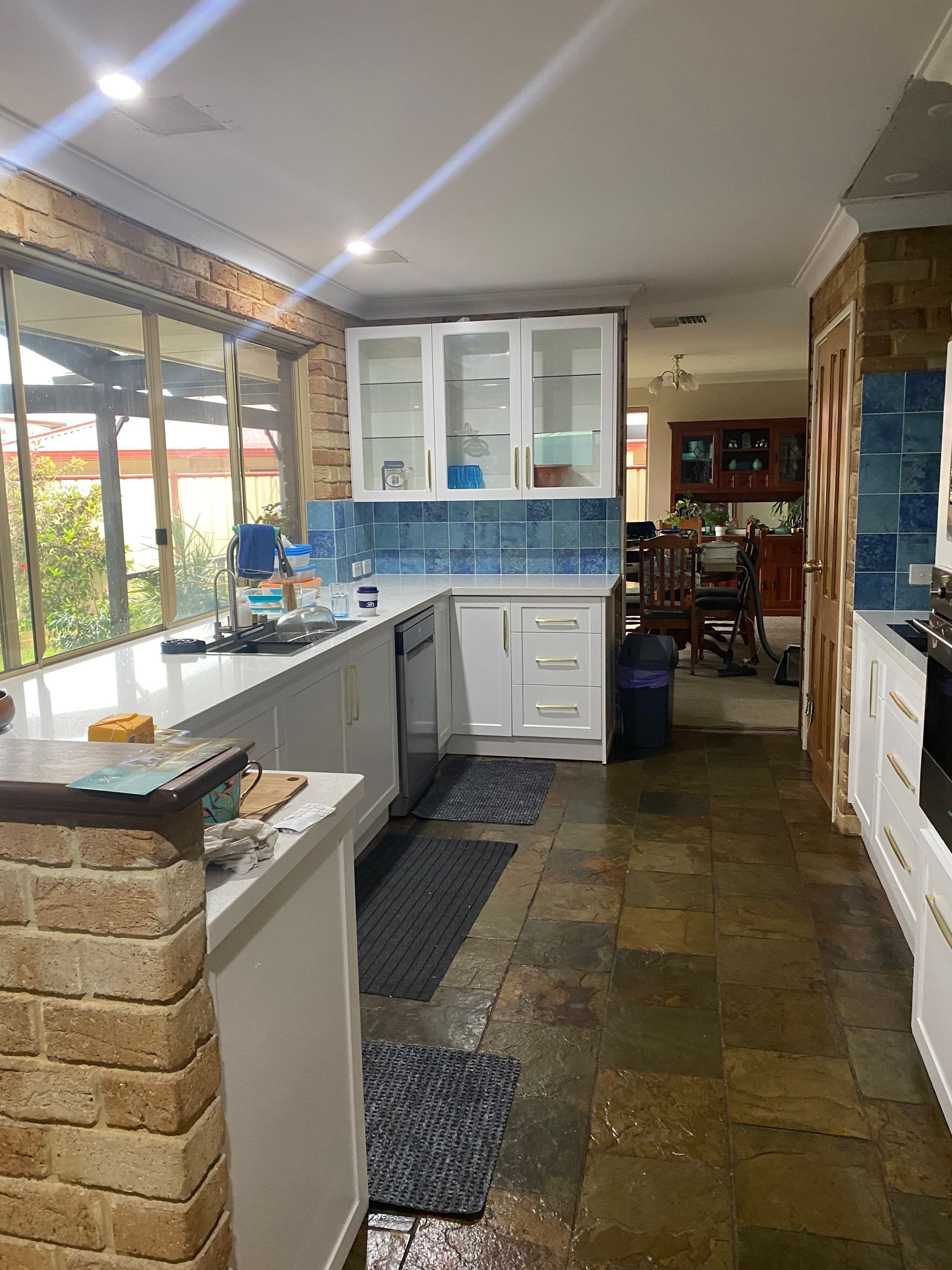 Kitchen with white cabinets, blue backsplash, and stone floor.