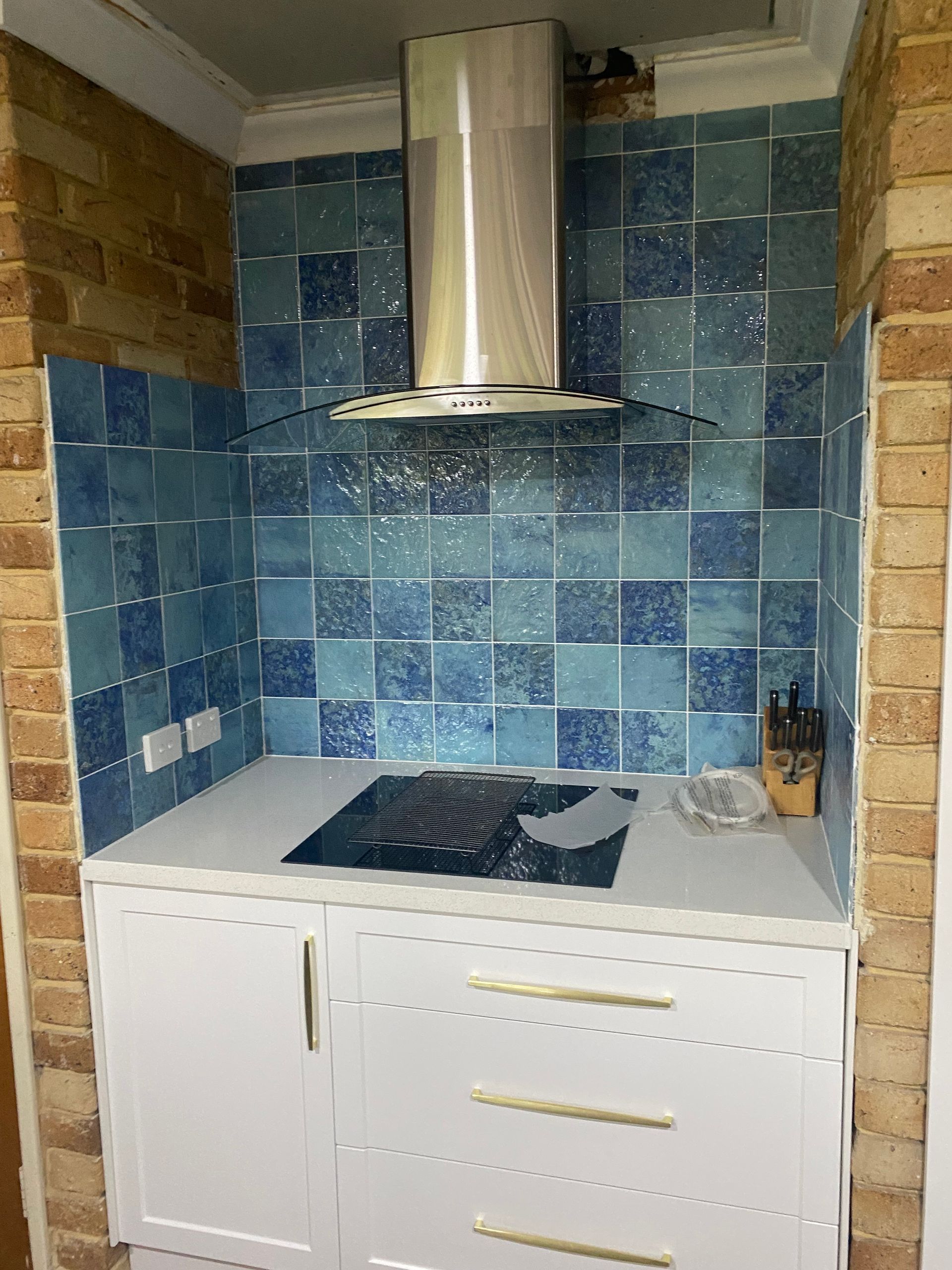 Kitchen niche with blue tiled backsplash, stainless steel vent hood, electric cooktop, and white cabinetry.