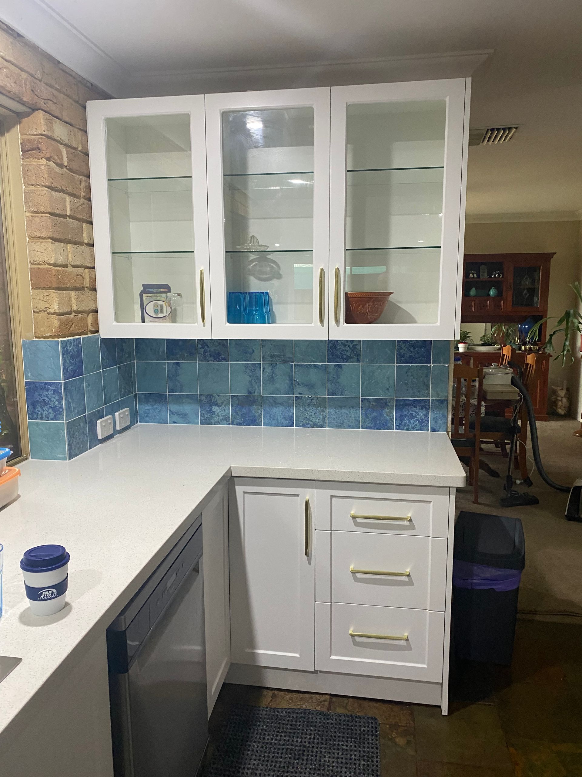 White kitchen cabinets with blue tile backsplash and gold hardware.