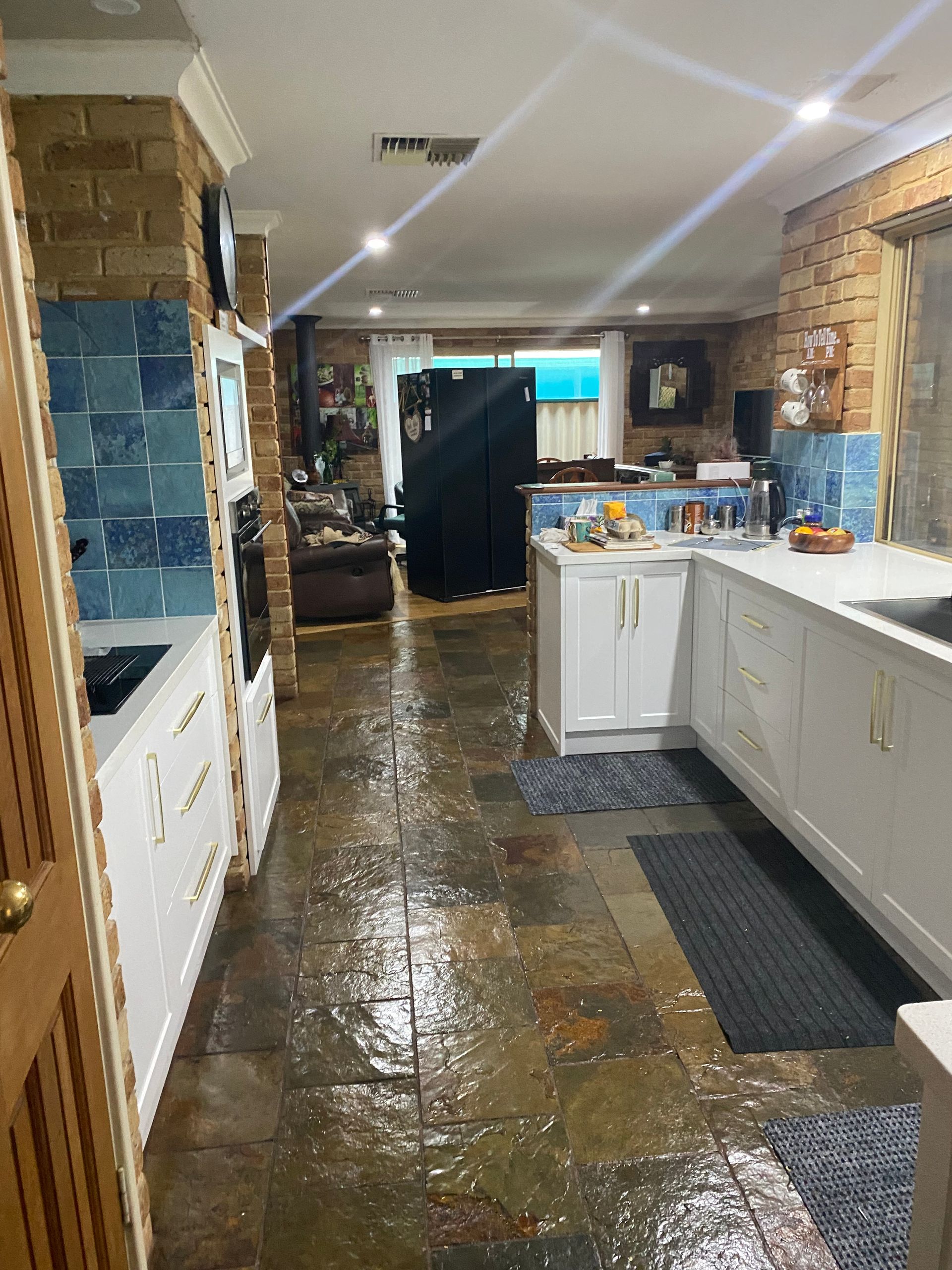 Flooded kitchen with white cabinets, blue backsplash, and stone tile floor; water damage.