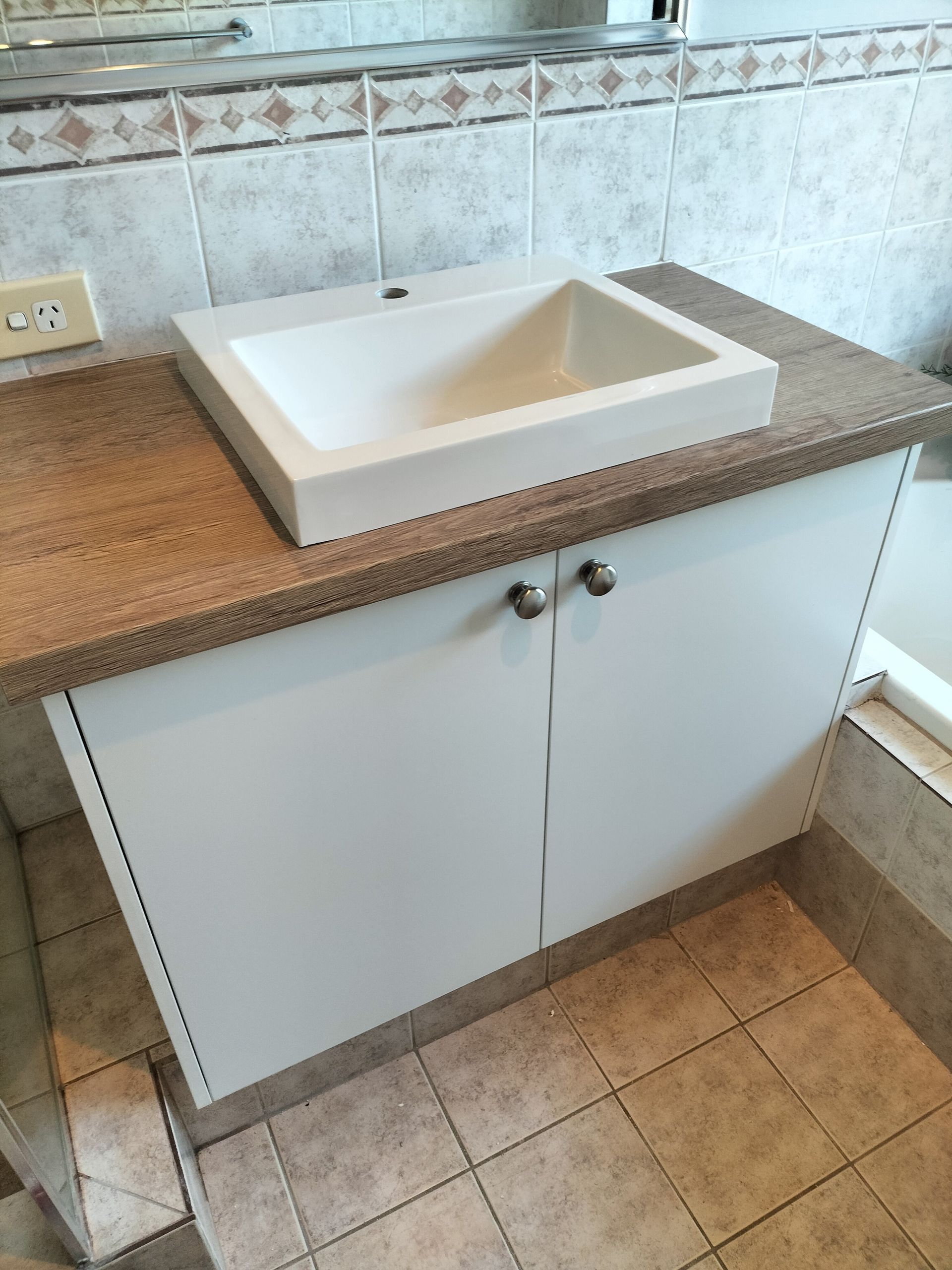 Bathroom vanity with white cabinet, brown countertop, and white rectangular sink.