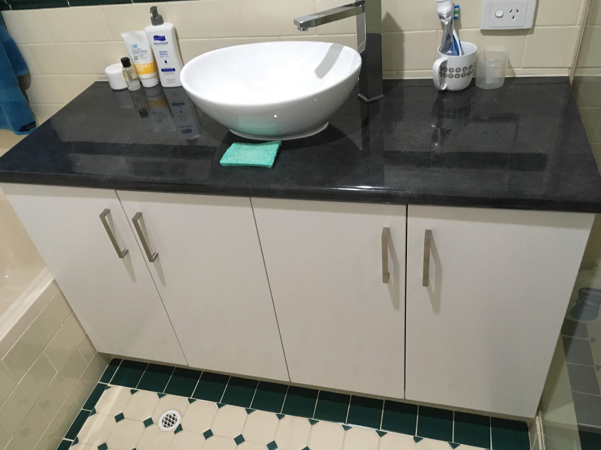 White vanity with black countertop, vessel sink, and chrome faucet. White cabinet doors with silver handles.